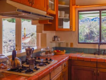 A cozy kitchen with wooden cabinets, a tiled countertop, and a view of mountains through the window.