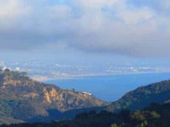 Panoramic view of a coastal landscape with hills and ocean under a cloudy sky.