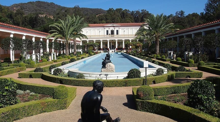 A serene garden with a long pool lined by palm trees and sculpted hedges.