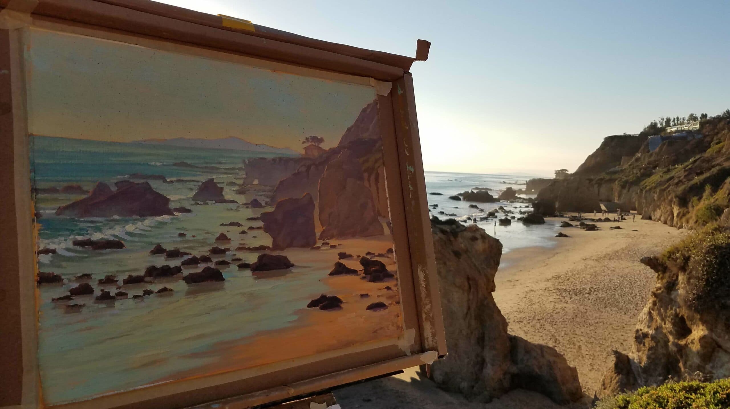 A landscape painting of a beach scene is displayed on an easel, with rocky shores and gentle waves in the background.