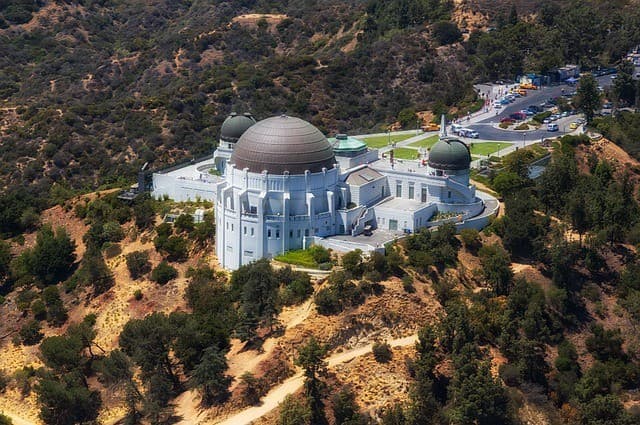 Aerial view of the Griffith Observatory surrounded by hills and trees.