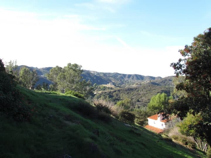 A scenic view of rolling green hills and a distant house under a clear blue sky.