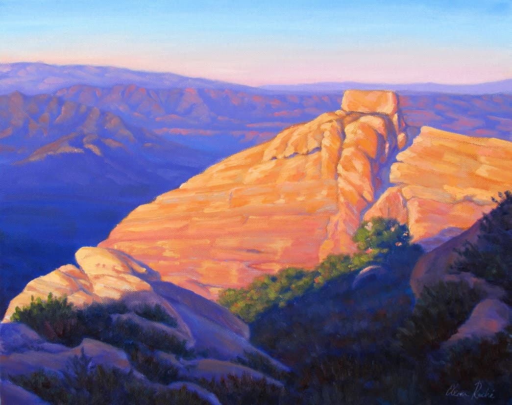 A vibrant sunset over a rocky landscape with layered mountains in the background.