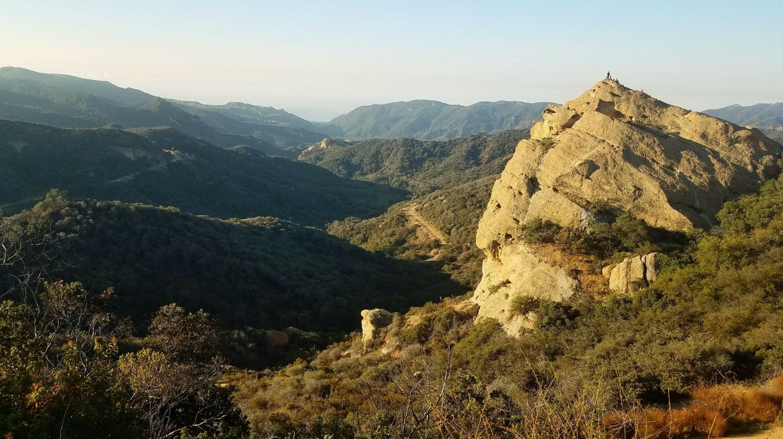 A scenic view of a rocky peak surrounded by rolling hills and valleys in the distance.
