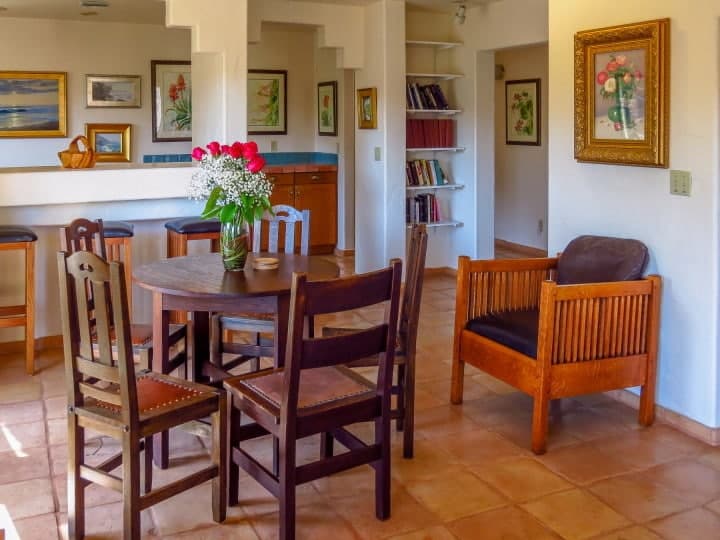 A cozy dining area with a round table, wooden chairs, a floral centerpiece, and art adorned walls.