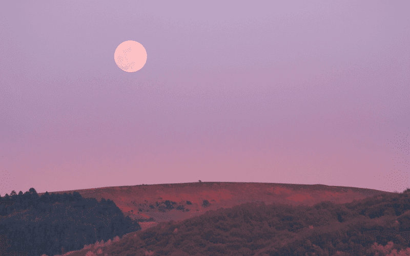 A full moon hangs over a softly lit landscape at dusk.