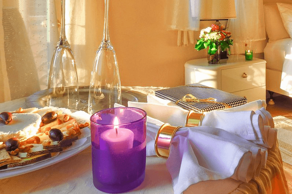 A cozy table setting featuring elegant glassware, a candle, a plate of snacks, and neatly arranged napkins.