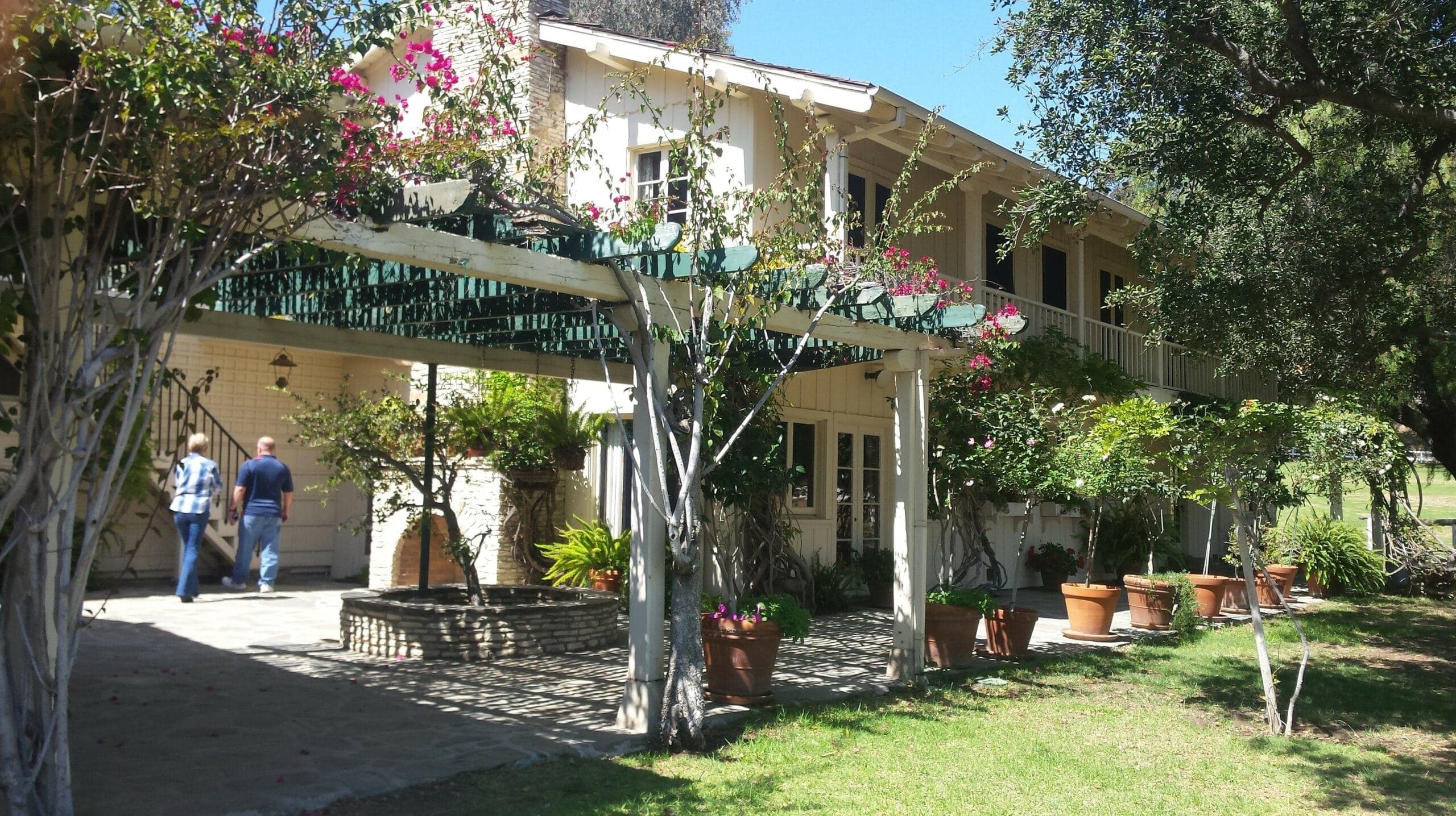 A house with a covered porch surrounded by potted plants and flowering vines.