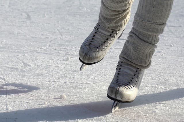 Close-up of a skater's feet wearing white ice skates on the ice.