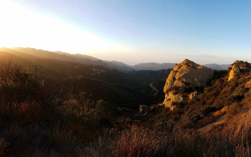 A panoramic view of rolling hills and rocky formations illuminated by a sunset. A panoramic view of rolling hills and rocky formations illuminated by a sunset.