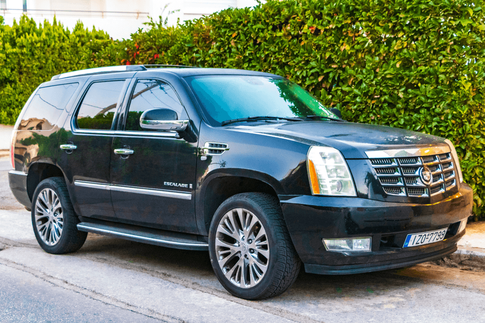 A black Cadillac Escalade parked on the street near green shrubbery.