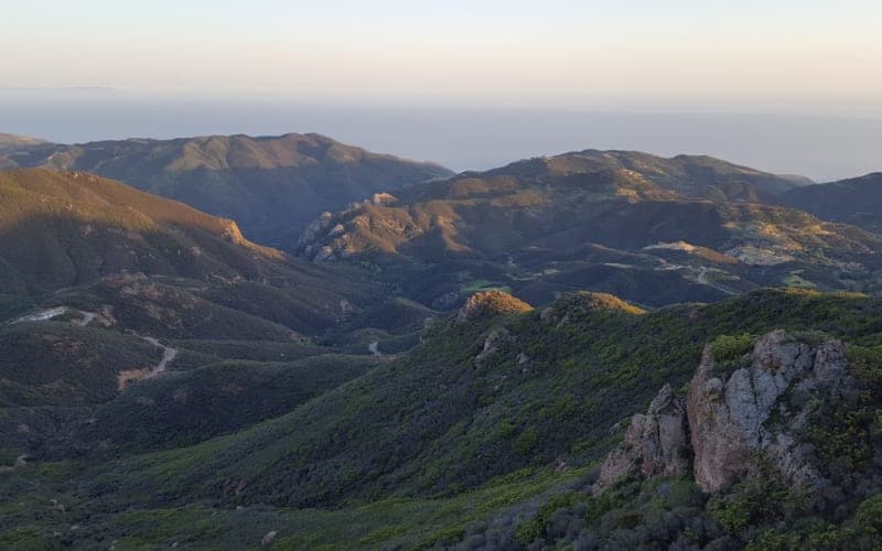 A panoramic view of rolling hills and mountains under a soft sunset glow. A panoramic view of rolling hills and mountains under a soft sunset glow.