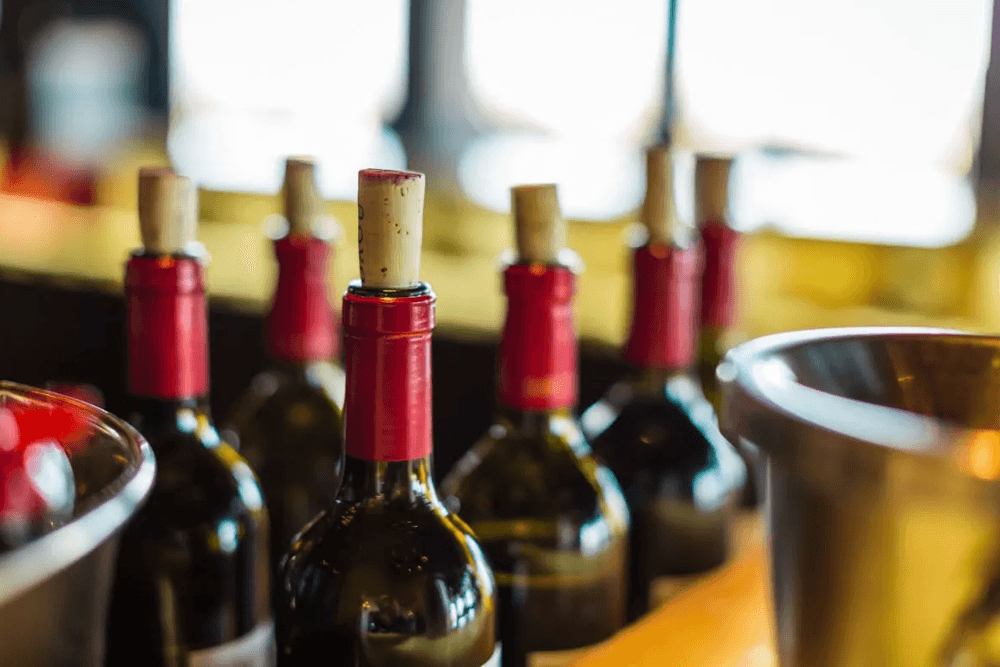 A row of wine bottles with red caps and corks on a bar.