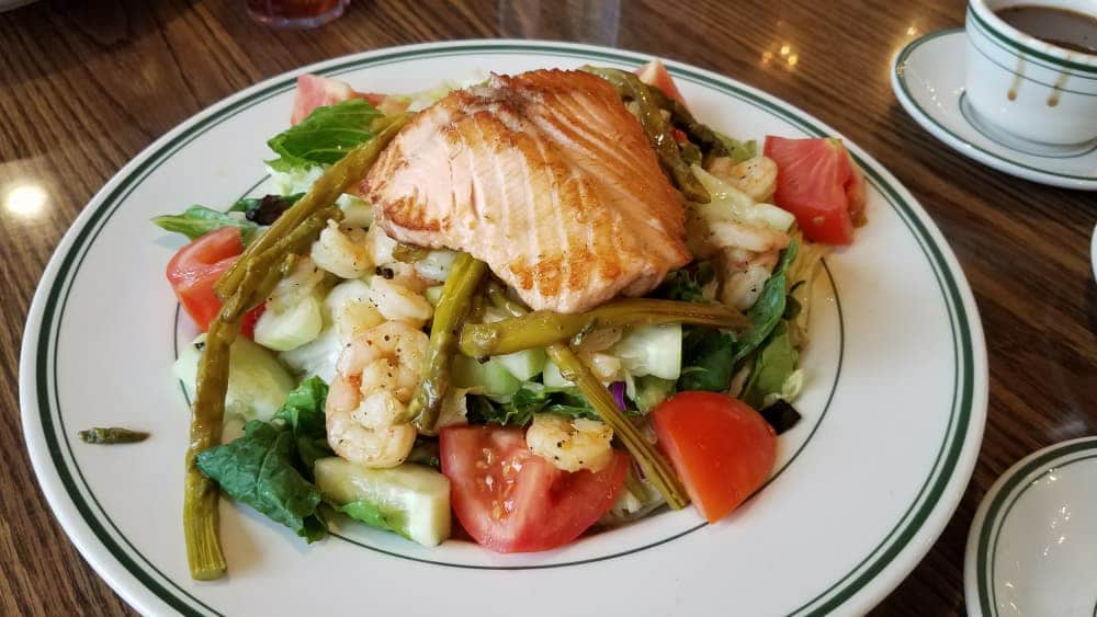 A plate of salad topped with grilled salmon, shrimp, asparagus, and fresh vegetables.