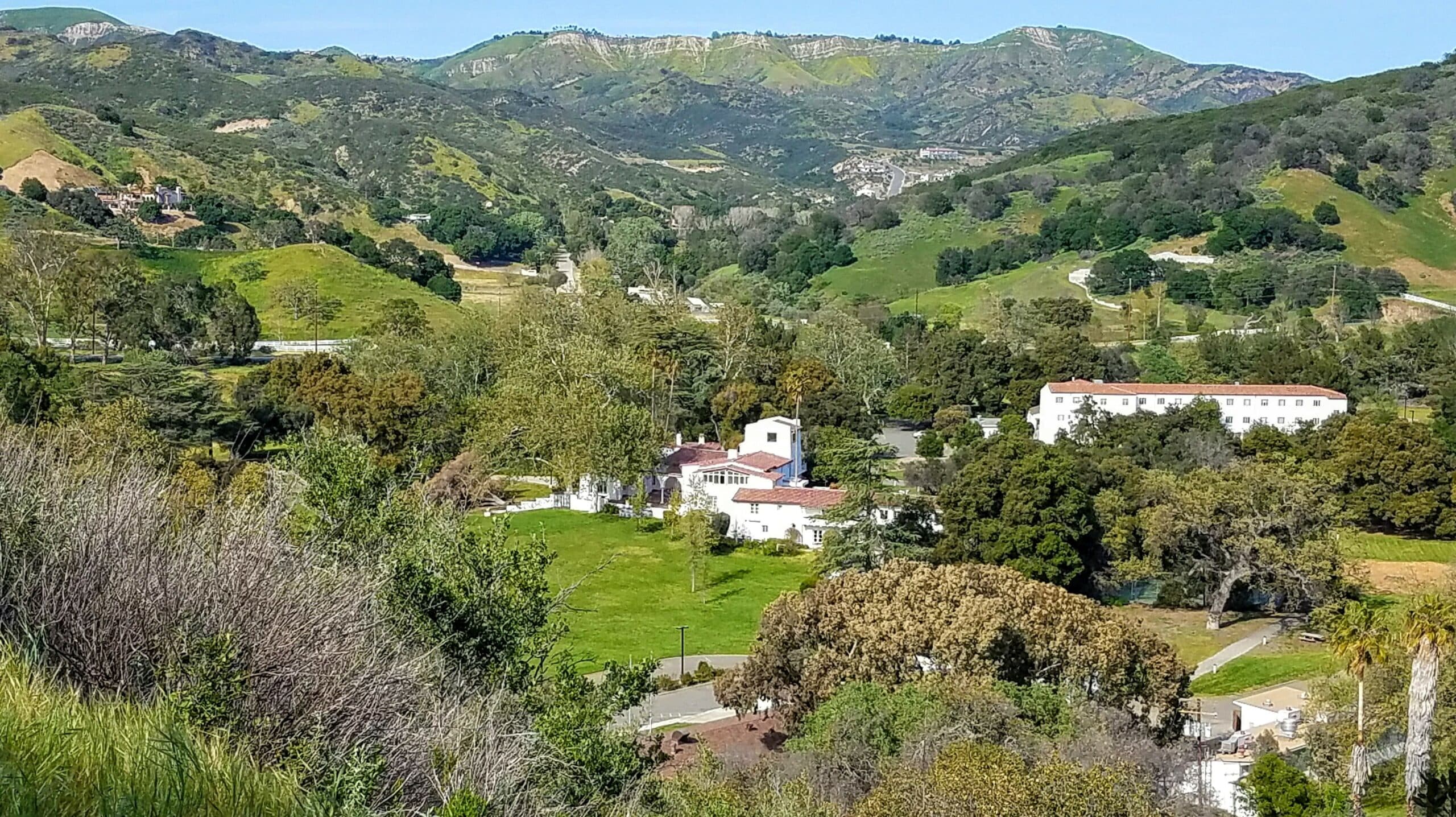A scenic view of rolling green hills with a white building and trees in the foreground.