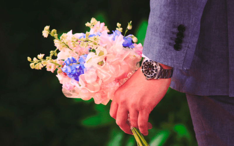 A person in a suit holds a bouquet of colorful flowers in one hand. A person in a suit holds a bouquet of colorful flowers in one hand.