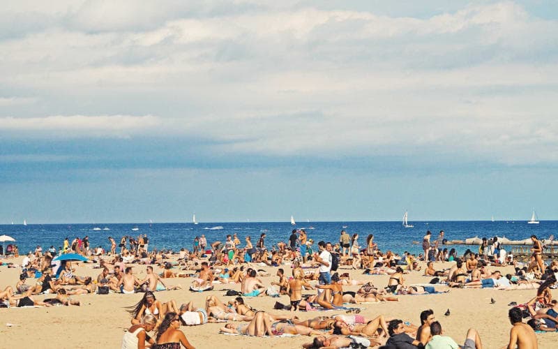 A crowded beach with people sunbathing under a partly cloudy sky. A crowded beach with people sunbathing under a partly cloudy sky.
