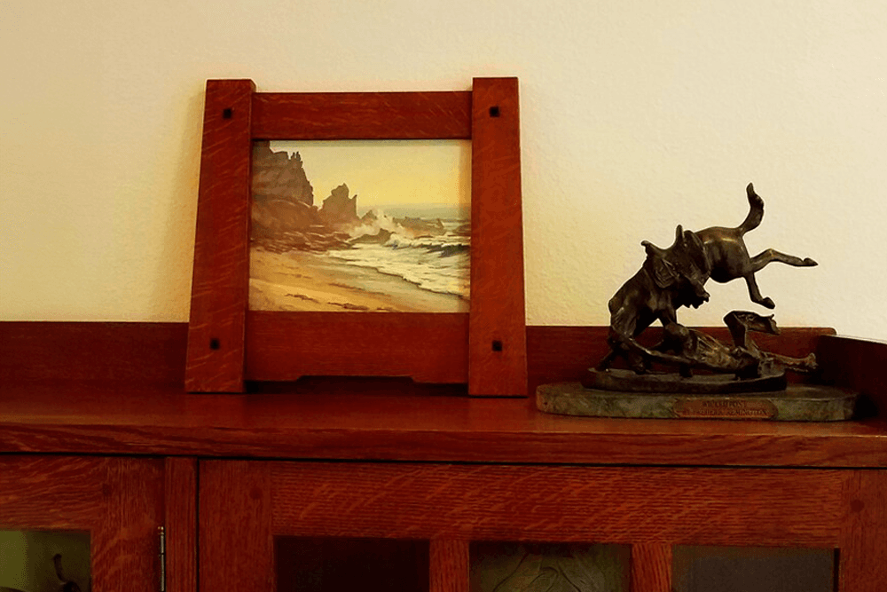 A framed seascape painting and a bronze sculpture of a dog on a wooden shelf.