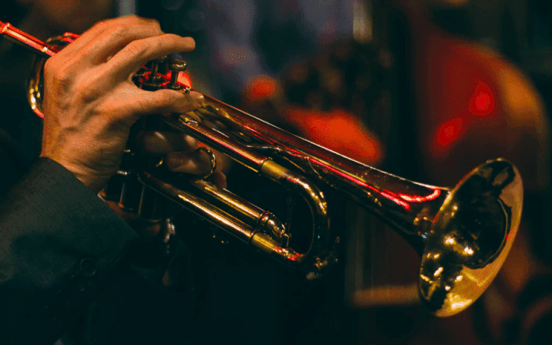 A hand holds a trumpet against a blurred background of musical instruments. A hand holds a trumpet against a blurred background of musical instruments.