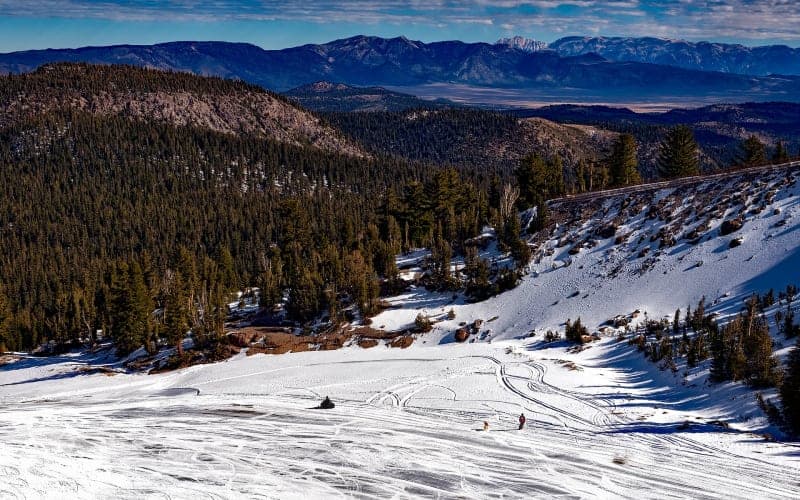 A snowy landscape with mountain views and ski tracks.