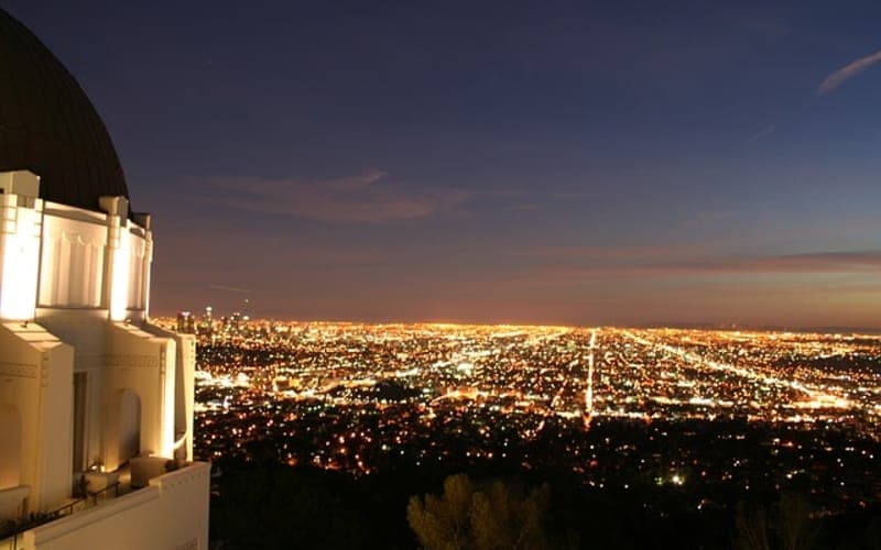 Night view of a city skyline illuminated by countless lights, with a prominent observatory in the foreground.